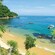 The view of a small beach from a forested hillside, with a few people and a fishing boat in the water